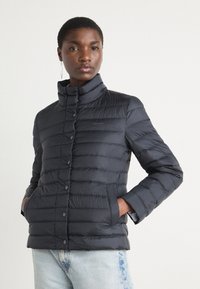 Padded black jacket with a high collar, front buttons, and side pockets, featuring stitched horizontal lines for texture. Brand logo visible.