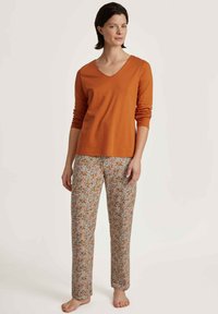 Oranje lange mouwen V-hals top gecombineerd met licht gekleurde bloemenpatroon broek van zachte stof. De outfit heeft een ontspannen pasvorm en taps toelopende benen.