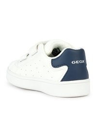 Baskets blanches avec un patch talon bleu marine, côtés perforés, bandes auto-agrippantes, et logo "GEOX" à l'arrière, vues de côté arrière.
