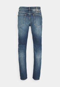 Jeans in denim blu da uomo con una vestibilità slim. Presentano due tasche posteriori e un'etichetta visibile in vita. Il tessuto mostra una leggera scoloritura.