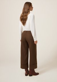 Witte blouse met lange mouwen, gecombineerd met bruine broek met wijde pijpen met een textuurpatroon en opgerolde mouwen, aangevuld met bruine enkellaarsjes.