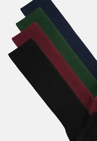 Conjunto de cuatro calcetines acanalados en negro, burdeos, verde y azul marino. Cada calcetín tiene una textura suave y una longitud uniforme.