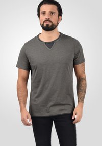 Grå t-skjorte med korte ermer og V-hals, med et lagdelt aksent ved halsen og en myk tekstur, brukt sammen med svarte jeans.