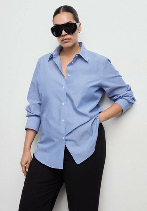 Blue and white striped button-up shirt with a collar and rolled sleeves, paired with black pants. Large black sunglasses as accessories.