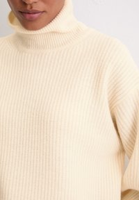 Roomkleurige geribbelde coltrui van textuurgaren, met een hoge kraag en een losse pasvorm.