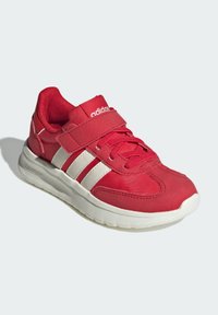 Červená športová topánka s bielym trojprúžkovým dizajnom, polstrovaným golierom a suchým zipsom. Má štruktúrovanú tkaninu a polstrovanú bielu podrážku.