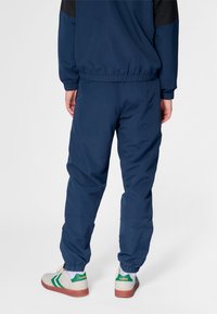 Mörkblå atletiska träningsbyxor med elastiska muddar och avslappnad passform, kombinerade med vita sneakers med gröna accenter.