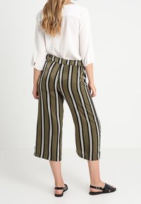 Pantalones cortos de color verde oliva con rayas verticales en blanco y negro. Fabricados con una tela suave, cuentan con una cinturilla elástica y bolsillos laterales.