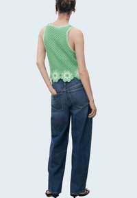 Top in cotone all'uncinetto di colore verde menta con dettagli floreali all'orlo, abbinato a jeans in denim blu scuro dal taglio morbido. Tessuto texturizzato e vestibilità ampia.