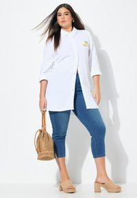 Camicia bianca con bottoni e maniche arrotolate; jeans blu a lunghezza caviglia; borsa a tracolla beige intrecciata; sandalini beige con tacco blocco.