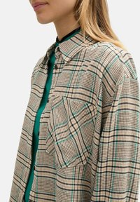 Camicia a quadri beige con un motivo a scacchi verde e nero, realizzata in tessuto testurizzato. Ha un collo con rever e dettagli su tasche.