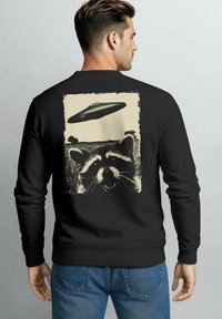 Black sweatshirt featuring a distressed graphic of a raccoon and a flying saucer on the back. Soft material with ribbed cuffs and hem.