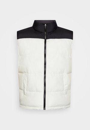 Veste sans manches matelassée avec épaules et col noirs, corps matelassé blanc, fermeture éclair avant et deux poches latérales.