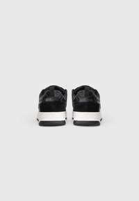 O pereche de sneakers Just Cavalli, alb-negru, fotografiată din spate pe un fundal alb simplu.