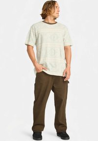 Vaaleanvihreä kuvioitu t-paita pyöreällä pääntiellä, yhdistetty ruskeisiin cargo-housuihin. Asu on rento ja siinä on teksturoitu kangas.