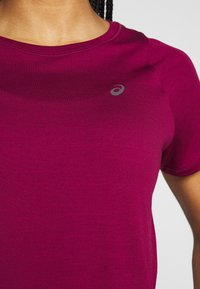 Camisa deportiva de manga corta en un vibrante magenta, hecha de un tejido suave y ligero. Presenta un pequeño logo gris en la parte superior izquierda.