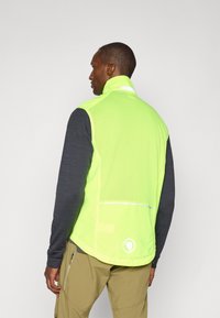 Neon green vest with mesh panels and reflective accents, paired with a dark gray long-sleeve shirt, back view. Solid color with no patterns.