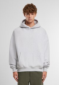 Svetlošedá mikina s kapucňou a predným vreckom, nastaviteľná šnúrka na kapucni a rebrované manžety. Vyrobená z jemnej textúrovanej látky. Voľný strih.