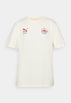 Valkoinen puuvillainen t-paitatakki, jossa on lyhyet hihat. Edessä on punainen Puma-logo ja brodeerattu FC Salzburgin vaakuna. Pyöreä pääntie.