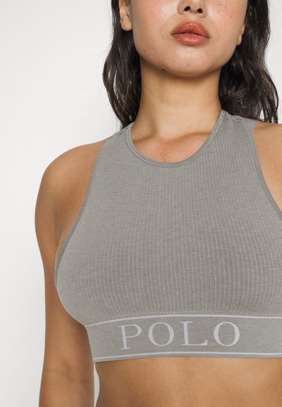 Pelēka ribota cropped blūze ar augstu apkakli un platām elastīgām lentes, uz kuras ir iespiests "POLO" gaiši pelēkā krāsā. Gluda tekstūra un pieguļošs dizains.
