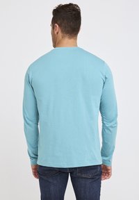 Lichtblauw langemouwen T-shirt van zachte stof, met een ronde hals en een rechte zoom, gecombineerd met donkerblauwe jeans.