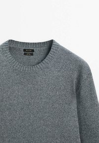 Pull gris en maille à col rond côtelé avec une étiquette noire cousue à l'intérieur de l'encolure.