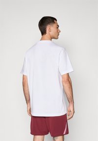 Witte katoenen t-shirt met korte mouwen en een ronde hals, gecombineerd met bordeauxrode shorts met een zijaccent in het roze. Eenvoudig ontwerp, zachte textuur.