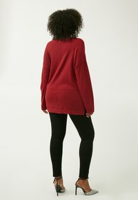 Maglione rosso oversize con spalle scese, maniche lunghe e orlo dritto, abbinato a leggings neri e scarpe con tacco argentate.