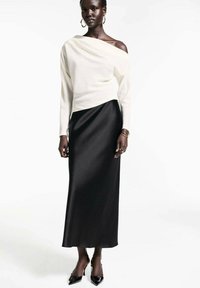 Top alb off-the-shoulder, asociat cu o fustă maxi din satin negru și fluidă. Modelul poartă tocuri negre și bijuterii simple.