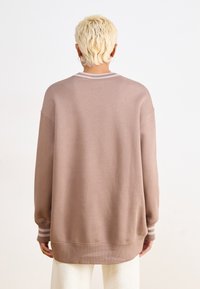 Felpa oversize beige con polsini e scollatura a coste, caratterizzata da strisce sobrie sui polsi e una texture di tessuto morbido.