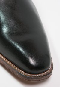 Chaussure de ville en cuir noir avec un bout pointu. Présente une finition brillante, une semelle en cuir cousue et un léger talon.