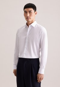 Biała koszula na guziki z małymi, ciemnymi kropkami, z kołnierzem typu spread i długimi rękawami, zestawiona z ciemnymi spodniami.