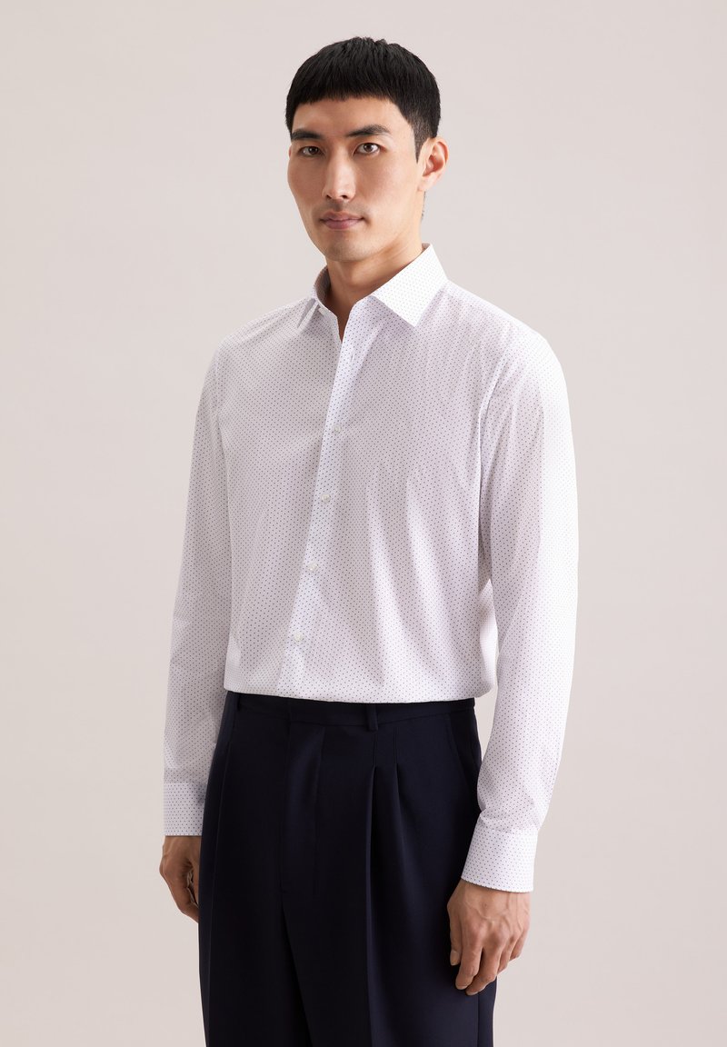 Biała koszula na guziki z małymi, ciemnymi kropkami, z kołnierzem typu spread i długimi rękawami, zestawiona z ciemnymi spodniami.