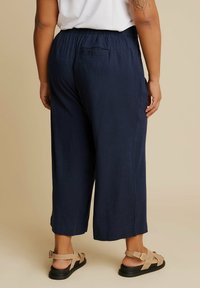 Granatowe spodnie o szerokich nogawkach z elastycznym pasem i tylną kieszenią, zestawione z beżowymi sandałami na paski na brązowym tle.