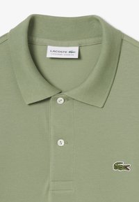Polo shirt verde chiaro in tessuto testurizzato. Presenta un colletto a costine, tre bottoni bianchi e un logo di coccodrillo ricamato.
