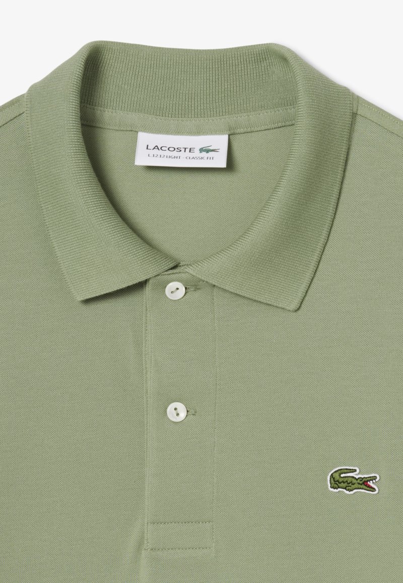 Light green polo shirt made of textured fabric. Features a ribbed collar, three white buttons, and an embroidered crocodile logo.