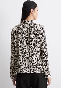 Leichte, cremefarbene Bluse mit schwarzem abstraktem Leopardenmuster, langen Ärmeln, geknöpften Manschetten und einem lockeren Schnitt. Flacher Kragen und Rückennaht-Detail.