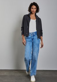 Tummanharmaa vetoketjulla varustettu takki, valkoinen hihaton paita, vaaleansiniset leveät farkut ja valkoiset lenkkarit. Sujuva rakenne, rento istuvuus ja vapaa-ajan tyyli.