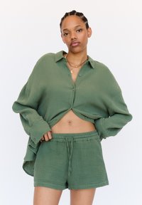 Green, textured cotton shirt with button closures and rolled sleeves, paired with matching shorts featuring an elastic waistband and drawstring.