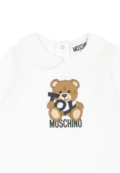 Camicia bianca in cotone con grafica di un orso che tiene il testo "TOY" e il nome del marchio "MOSCHINO" sotto in nero. Colletto arrotondato.