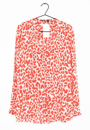 Langærmet, knappet bluse med rød og hvid leopardmønstret print, hængende på en sort bøjle.