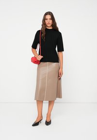 Zwarte geribbelde trui met korte mouwen, beige faux leren midi rok met een naad in het midden, rode clutch tas en zwarte puntige hakken.