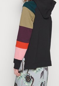 Felpa con cappuccio di colore nero, maniche multicolori a contrasto in oliva, bordeaux, arancione, rosa e blu navy. Realizzata in morbido cotone.