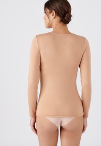 Maglietta aderente a maniche lunghe in beige chiaro, texture liscia, scollo rotondo, con sottili dettagli di cucitura, abbinata a biancheria intima color nudo.