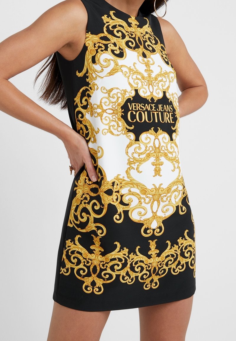 Robe noire sans manches avec centre blanc, motifs baroques dorés ornés et texte "Versace Jeans Couture" à l'avant.
