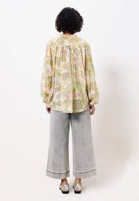 Blouse à manches longues avec motif floral dans des couleurs pastel, associée à un pantalon en denim gris clair à jambes larges et des chaussures métalliques argentées.