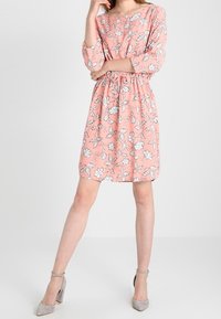 Rosa blommig klänning med trekvartslång ärm, samlad midja och en avslappnad passform. Har vita blommönster på ett texturerat tyg.