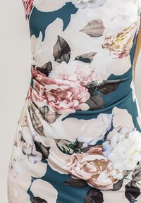 Abito con stampa floreale che presenta grandi rose in tonalità di rosa e bianco su uno sfondo teal. Tessuto morbido e elasticizzato con un effetto drappeggiato.