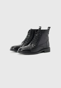 Botas de cuero negro hasta el tobillo, con puntera redonda, cordones, costuras en el panel lateral y un tacón bajo estilo bloque. Incluye una tira en la parte posterior para ayudar a ponérselas.
