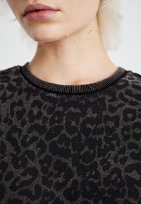 Czarny i szary sweter w panterkę z ribbowanym dekoltem, charakteryzujący się miękką teksturą i wyraźnym wzorem zwierzęcym w całym fasonie.